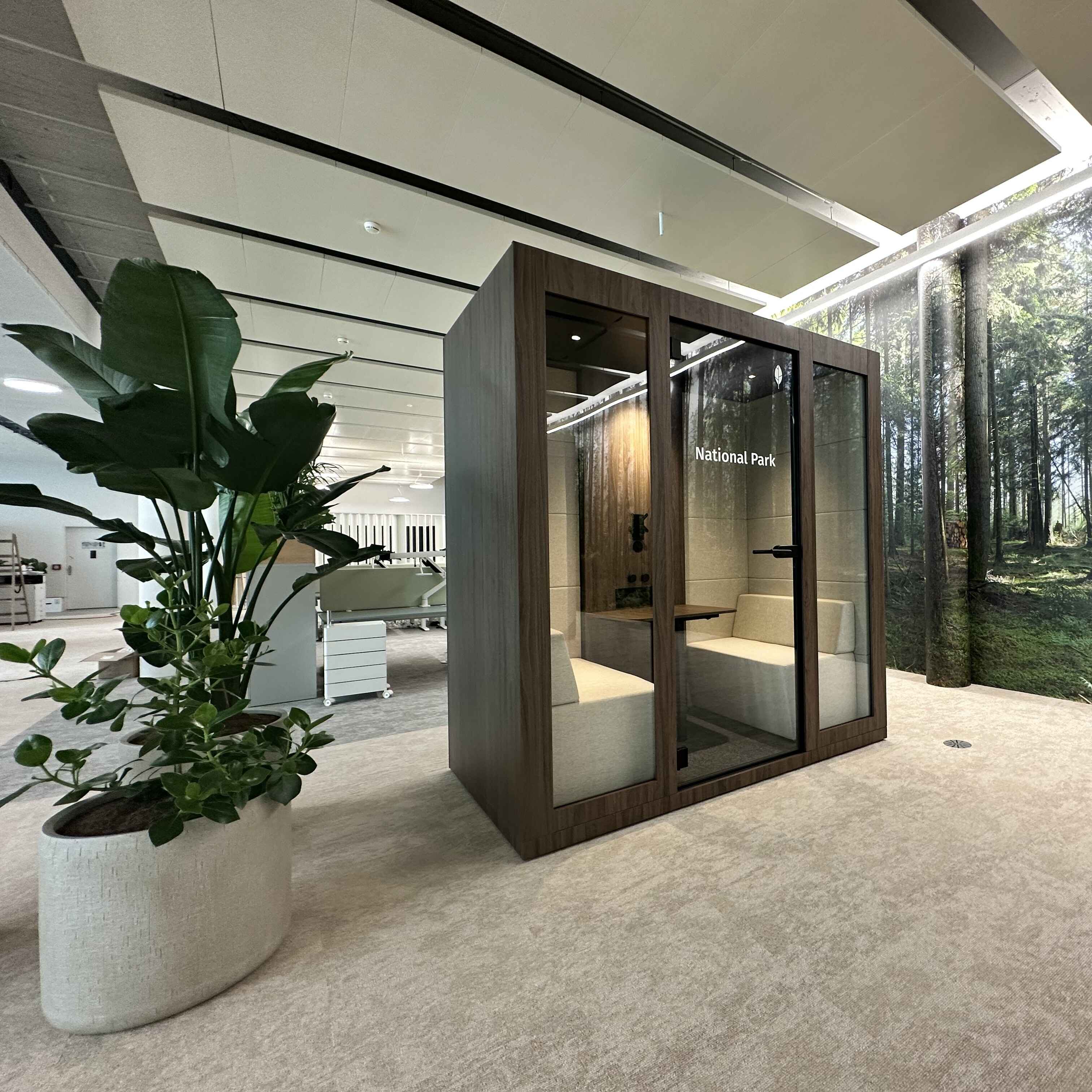 Besprechungsbox Silent Room M mit zwei Personen im Gespraech – akustisch abgeschirmte Kabine mit gepolsterten Sitzbaenken und Tisch fuer effiziente Teammeetings im Buero