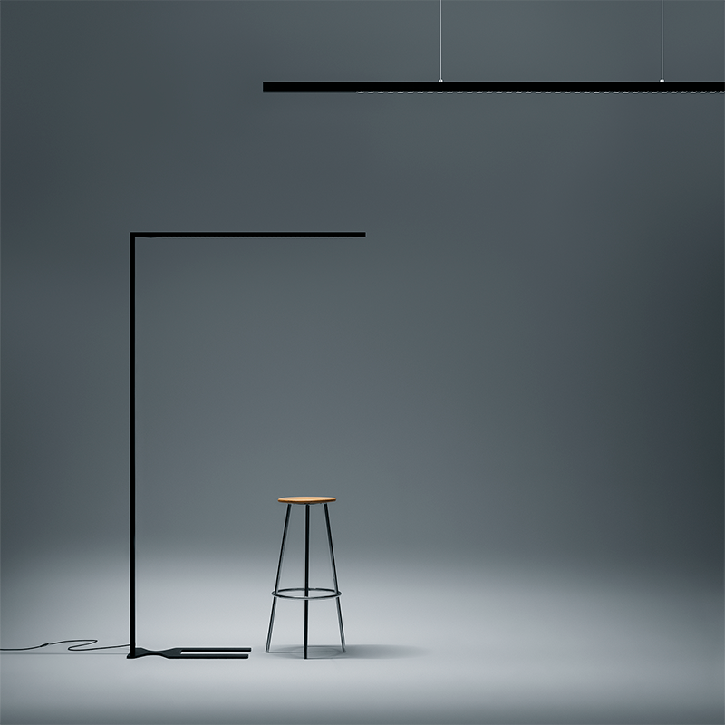 Zumtobel LINETIK Pendel- und Stehleuchte in Schwarz mit schlanken Leuchtenprofilen neben einem Hocker.