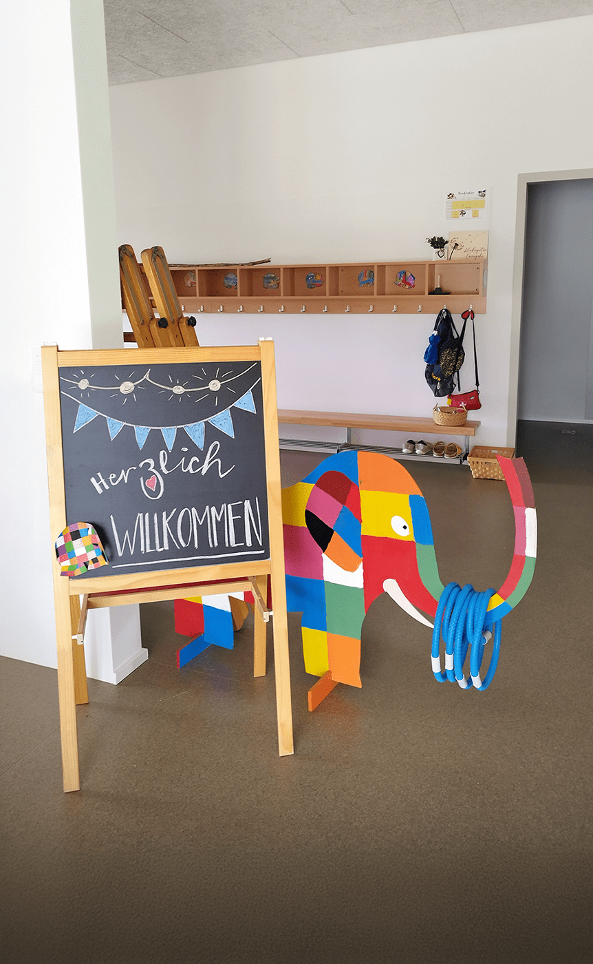 Modern eingerichteter Kindergartenraum mit funktionalen Moebeln, darunter Tische, Stuehle und Regale in warmen Holztoenen, gestaltet fuer eine einladende und kindgerechte Umgebung, praesentiert von Kibemo