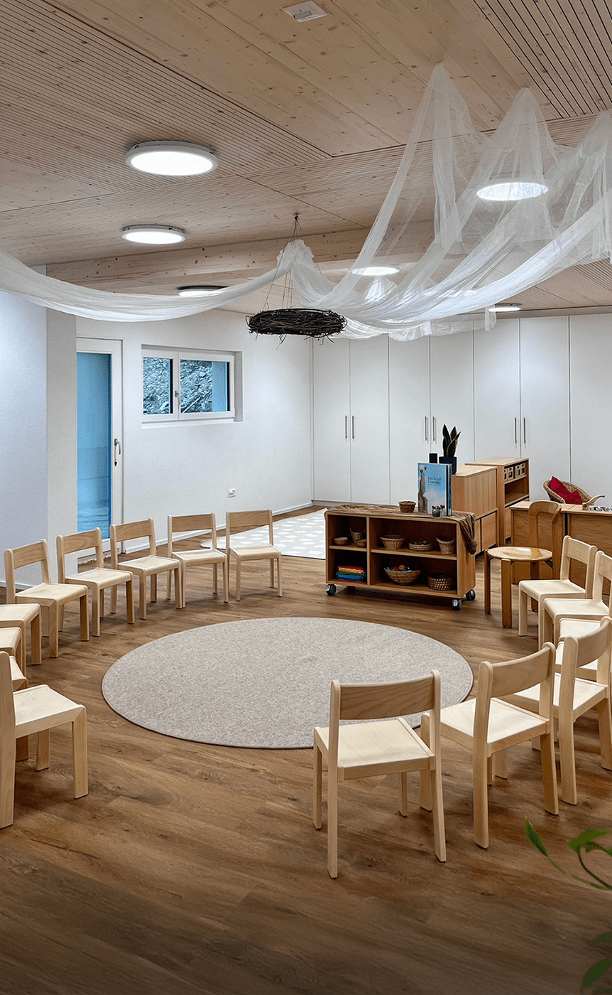 Kindergartenraum mit natuerlichen Holztischen, farbenfrohen Stuehlen und vielseitigen Regalen, gestaltet fuer eine warme und einladende Atmosphaere, praesentiert von Kibemo
